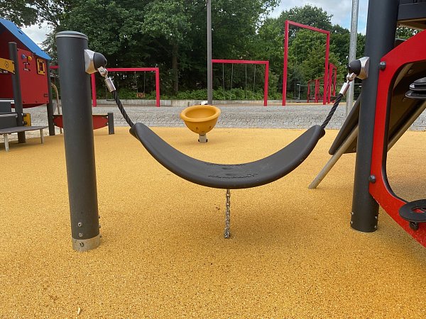 Der Pendelsitz ist besonders niedrig, damit ihn auch Kinder mit Einschränkungen zum Spielen nutzen können. Im Hintergrund ist eine leicht geneigte gelbe Drehschüssel zu sehen. - © Markus Voss