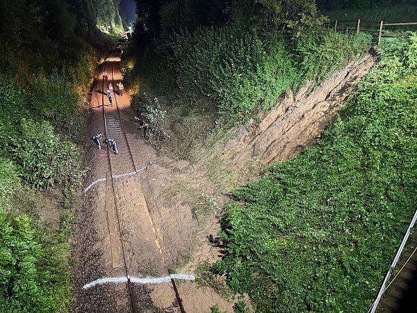 Erde liegt nach einem Hangrutsch auf den Gleisen, im Hintergrund ist der entgleiste Regionalexpress auf der Strecke zu sehen. - © Nico Pointner/dpa