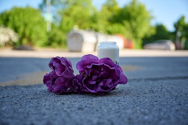 Blumen und eine Kerze liegen auf einem Schotterplatz vor dem Eingang zu einem Spielplatz in Menden, wo ein 14-Jähriger ums Leben kam. - © Bernd Thissen/dpa