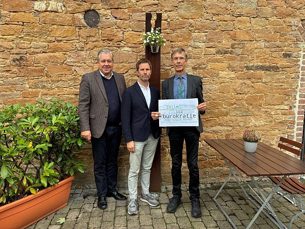 Christoph Barre (v. l.) und Jan Christoph Weitkamp mit Karl-Ernst Hunting (Leiter der Mindener IHK-Zweigstelle), der ein Plakat hält mit den von den Unternehmen genannten größten Risiken für die wirtschaftliche Entwicklung der kommenden zwölf Monate. - © IHK Ostwestfalen