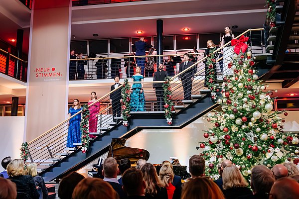 Neue Stimmen im Advent: Die Masterclass-Teilnehmenden auf der Treppe im weihnachtlich geschmückten Foyer der Bertelsmann-Stiftung. Eine Etage darüber begleiten Blechbläser des Luftwaffenmusikkorps Münster unter Oberstleutnant Alexander Kalweit. - © BESIM MAZHIQI