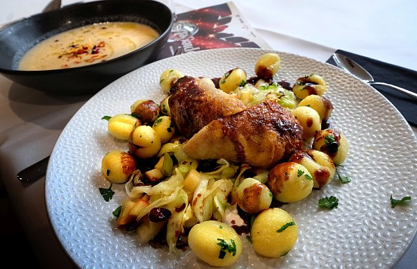 Roulade vom Kikok-Huhn auf mildem Pfefferjus mit Kräutergnocchi und Apfel-Cranberry-Spitzkohl. Im Hintergrund die vegane Apfel-Sellerie-Cremesuppe. - © Andreas Frücht