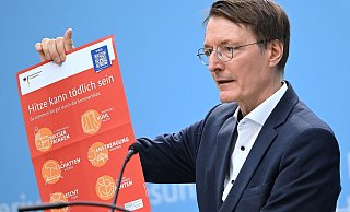 Bundesgesundheitsminister Karl Lauterbach (SPD) hält ein Plakat zum Thema Hitzeschutz hoch. - Britta Pedersen/dpa