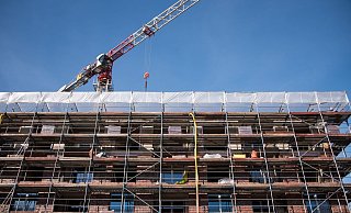 Ein Gerüst ist auf einer Baustelle an einem Neubau von einem Mehrfamilienhaus installiert, über dem Gebäude ist ein Baukran zu sehen. - Foto: Daniel Bockwoldt/dpa
