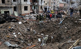 Rettungskräfte stehen neben einem Krater in der Nähe beschädigter Wohngebäude nach einem russischen Raketenangriff. - -/Ukrinform/dpa