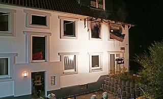 Durch ein Feuer brannte eine Wohnung im ersten Stock dieses Mehrfamilienhauses an der Altenbekener Burgstraße komplett aus. Feuerwehrleute werfen gerade ein Möbelstück aus dem Fenster in den Garten. - Ralph Meyer