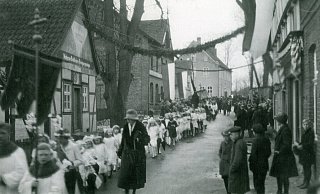 Kommunionkinder ziehen am Hochzeitshaus (l.) vorbei. Maria Welschof, Lehrerin an der Brinkschule, begleitet sie. Neben dem Hochzeitshaus stand Peters Eiche, dahinter das Gasthaus „Kösters" und die Jungen- oder Kirchschule. Das Gebäude rechts ist die heutige Tor-Deele. Die Aufnahme ist wohl aus dem Jahr 1938. - Fotosammlung Potthoff