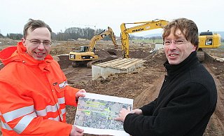 Projektleiter Tobias Fischer (l.) und Andreas Meyer (r.) mit dem Plan des ersten Bauabschnitts der Nordumgehung. Im Hintergrund entsteht ein Regenrückhaltebecken. - Foto: Jörg Stuke