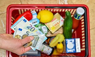 Eine Frau hält auf ihrer Hand Geldscheine vor einem Korb mit Einkäufen - Patrick Pleul/dpa
