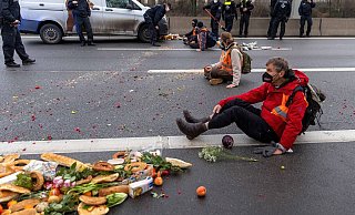 Klimaaktivisten der Gruppe «Aufstand der letzten Generation» sitzen auf der Fahrbahn und blockieren den Verkehr. - Foto: Carsten Koall/dpa