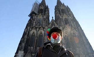 Lorenz steht mit Clownsnase auf der Maske vor dem Kölner Dom. - Foto: Oliver Berg/dpa
