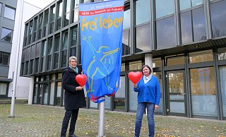 Bürgermeisterin Susanne Rutenkröger (links) und Gleichstellungsbeauftragte Dorit Bethke hissen die Fahne „Nein zu Gewalt an Frauen!“ auf dem Rathausplatz. - Stadt Bünde
