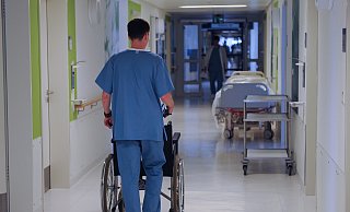 Ein Pfleger schiebt mit einen Rollstuhl über einen Flur.  - picture alliance / dpa