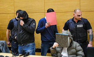 Der Hauptangeklagte passiert hinter einer Aktenmappe versteckt, die beiden Mitangeklagten. - Andreas Zobe