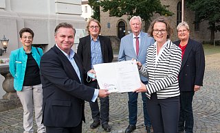 Ministerin Ina Scharrenbach überreicht den Förderbescheid an Bürgermeister Tim Kähler. Mit ihm freuen sich die Gleichstellungsbeauftragte Karola Althoff-Schröder (hi. v. l.), die stellvertretenden Bürgermeister Andreas Rödel und Werner Seeger sowie Birgitt Fischer, Vorsitzende des Kulturbeirates. - Ralf Bittner