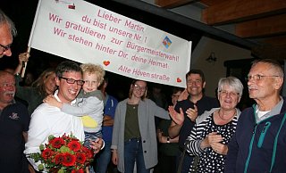Martin Hoffmann mit Sohn Linus auf dem Arm (er wollte noch wachbleiben) und Freunden und Nachbarn, die für ihren Wahlsieger ein besonderes Banner gestaltet haben. - Knut Dinter