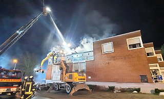 Während ein großer Bagger mit Greifer Teile des verkohlten Daches der Nieheimer Sparkasse herunterholt, wird das Feuer von Drehleitern aus gelöscht. - David Schellenberg