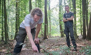 Förster Julian Schütz hebt mit dem Messer ein Stück Rinde von der wegen Borkenkäferbefalls gefällten Linde. Gemeinsam mit Ralf König führt er die Gruppe durch den Stadtwald. - Ralf Bittner