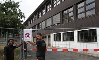 Absperrung: Bauarbeiter bringen ein Schild "Betreten verboten" am Bauzaun an, der rund um den Altbau steht. Das Schulgebäude wird jetzt komplett eingerüstet. - Diete Scholz