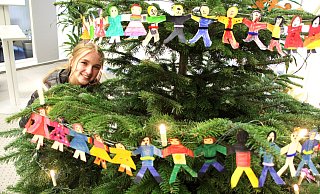 Eine 20 Meter lange Menschenkette ringelt sich um diesen Weihnachtsbaum in der Volksbankfiliale in der Kalandstraße, den Jurymitglied Sophia (16) präsentiert. Gestaltet wurde er von 18 Warburger Flüchtlingskindern. - Burkhard Battran