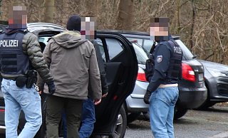 Beamte führen einen Mann zu einem Zivilfahrzeug. Offenbar handelt es sich um eine Festnahme. In welcher Beziehung der Mann zu der Plantage steht, ist derzeit noch unklar. - Moritz Trinsch