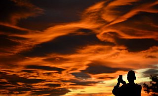 Das Naturschauspiel festhalten: Ein Mann fotografiert einen Sonnenuntergang. - Laurent Gillieron/KEYSTONE/dpa