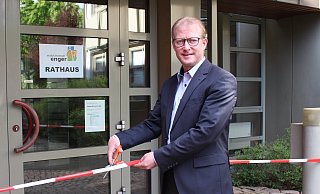Bürgermeister Thomas Meyer macht einen symbolischen Schnitt durchs Absperrband: Ab dem 11. Mai ist das Rathaus wieder für Bürger persönlich erreichbar – zunächst jedoch nur mit Termin. - Stadt Enger