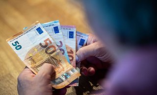 Ein älterer Mann sitzt an einem Tisch und zählt Geld. - Lino Mirgeler/dpa