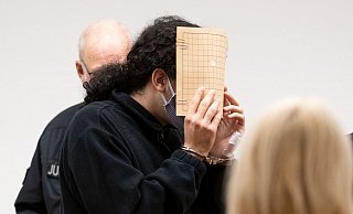 Der Angeklagte (M) hält sich im Saal des Landgerichts eine Aktenmappe vor das Gesicht. - picture alliance/dpa