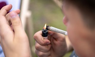 Ein junger Mann zündet sich einen Joint an – die Debatte um die Cannabis-Legalisierung in Deutschland spitzt sich wieder zu. - picture alliance/dpa