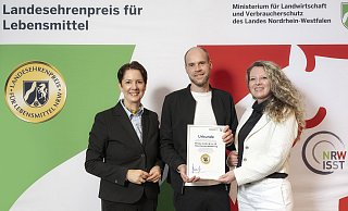 Landwirtschaftsministerin Silke Gorißen (links) überreicht Marketing-Leiter André Hilker und seiner Kollegin Natali Willms (stellvertretende Leitung Qualitätsmanagment und Umwelt- und Energiebeauftragte) den Landesehrenpreis für Lebensmittel NRW 2025. - www.fotografie-coscia.de