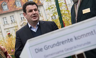 Hubertus Heil (SPD), Bundesarbeitsminister , besucht ein Mehrgenerationenhaus und steht vor einem Wegweiser, auf dem "Die Grundrente kommt!" steht. - picture alliance/dpa