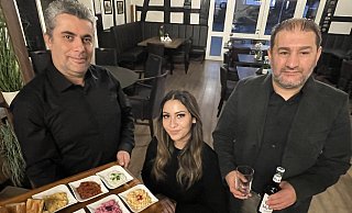 Die beiden Betreiber Bilgin Celik (l.) und Veysel Dinc servieren einer Kundin Vorspeisen und ein Getränk. - Elke Niedringhaus-Haasper
