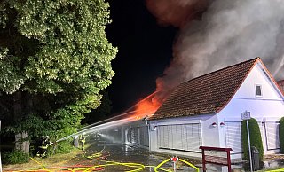 Feuerwehrleute bekämpfen die Flammen, die immer wieder aus dem Dach der Lagerhalle auflodern. Foto: Thorsten Heß - Thorsten Heß