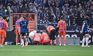 Joel Grodowski (Arminia Bielefeld) muss nach einem Zusammenprall mit Schalkes Torwart Loris Karius behandelt werden. - KROEGER/RHR-FOTO