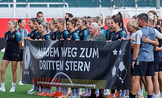 Die deutschen Spielerinnen stehen beim Abschlusstraining mit einem Banner für ein Gruppenfoto auf dem Platz. - Daniel Karmann/dpa