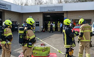 Einsatzkräfte stehen in Bereitschaft, während weitere Feuerwehrleute die Innenräume der Autowerkstatt erkunden - Ralph Meyer