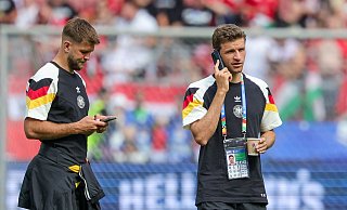 Deutschlands Thomas Müller (r) steht telefonierend mit einem Getränk auf dem Rasen, neben ihm Niclas Füllkrug. - Christian Charisius/dpa