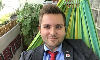 Pierre Schelper ist Vorsitzender der Partei Die Partei im Kreis Paderborn und Mitglied des Stadtrates. Dass er für dieses Foto in einer Hängematte liegt, gehört zur satirischen Selbstdarstellung. - Die Partei