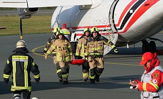 Einsatzkräfte der Feuerwehr tragen einen Verletzten, der bei der Notfallübung aus dem Flugzeug gerettet wurde, zur Sammelstelle. - Ralph Meyer