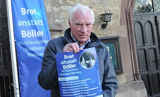 An einem Fahnenmast auf dem Brüderkichhof zwischen den Städten weht die neue Fahne der Aktion "Brott anstatt Böller". Mitinitiator Christian Voß präsentiert das Plakat, das aufmerksam machen soll. - Hubert Rösel