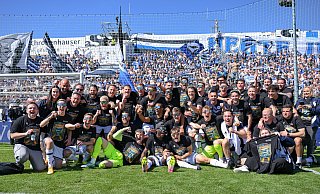 Spieler, Trainer und Mitarbeiter von Arminia Bielefeld genießen die ausgelassenen Aufstiegsfeierlichkeiten im Sportpark Unterhaching vor den mitgereisten Fans. - Teresa Kroeger/RHR-FOTO