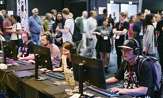 Besucher der Gamescom testen die neuesten Spiele-Highlights an PC-Stationen, während im Hintergrund zahlreiche Messebesucher die Hallen erkunden. - Koelnmesse GmbH/Marvin Ruppert