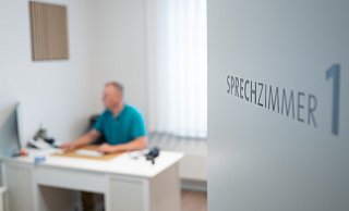 Ein Hausarzt sitzt in einem Sprechzimmer seiner Hausarztpraxis an einem Schreibtisch und arbeitet am Computer. - Neue Westfälische