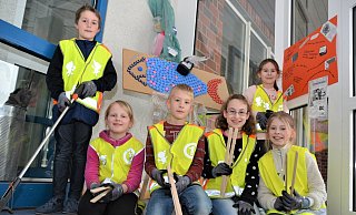 Die OGS-Kinder Bo, Lena, Mika, Guilia, Celina und Julia (v. l.) haben schon einmal ihre Warnwesten übergezogen. Mit Zangen werden sie beim Müllsammeln helfen. Im Hintergrund ist ein von den Schülern gestalteten Fisch aus Flaschendeckeln und anderem Abfall zu sehen. - Karin Prignitz