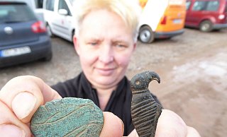 Prunkstücke aus der Siedlung: Andrea Goernemann, Mitarbeiterin des Grabungsteams, zeigt eine Brosche mit stilisierten Tierfiguren und eine Gewandnadel in Vogelform. - Sven Spiong/LWL