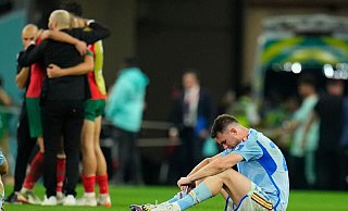 Spaniens Aymeric Laporte sitzt nach der Niederlage auf dem Spielfeld, während Marokkos Spieler im Hintergrund über ihren Sieg im Elfmeterschiessen jubeln. - Julio Cortez/AP/dpa