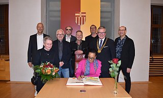 Sängerin Carmen Purperhart (Mitte) trägt sich ins Goldene Buch der Stadt Paderborn ein, mit dabei: Keyboarder Ferdinand Brüggemann (hinten v.l.), Witwe des Sängers Egon Ingeborg Bielawny, Gitarrist Peter Lemanski, Bassist Helmut Protte, Produzent Migo Fecke, Texter Stephan Ehritt, Bürgermeister Michael Dreier sowie Schlagzeuger und Sänger Jörg Putze. - Stadt Paderborn/Veronika Kinsfato