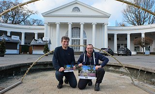 Tammo Ulrich (l.) und Olaf Edler vor der Wandelhalle im Kurpark mit ihrem neuen Kurstadt-Wandkalender 2026. - Ulf Hanke