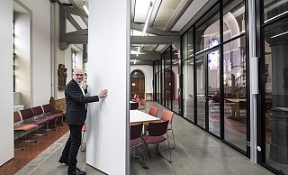 Pfarrer Christoph Steffen demonstriert, wie man mit Hilfe einer Trennwand mehrere Räume unter der Empore erhält. - © Jörg Dieckmann -www.dieckmann-fotodesign.de